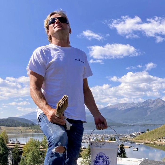 Jiri on a rooftop job in the Colorado mountains, holding a brush and paint bucket